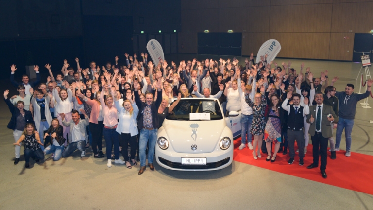 Große Gruppe von Menschen feiert vor einem VW Auto
